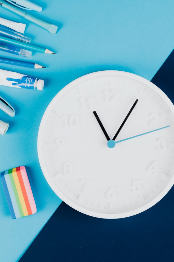 School supplies and a white clock arranged on a blue background, representing preparation and time management for the new school year.
