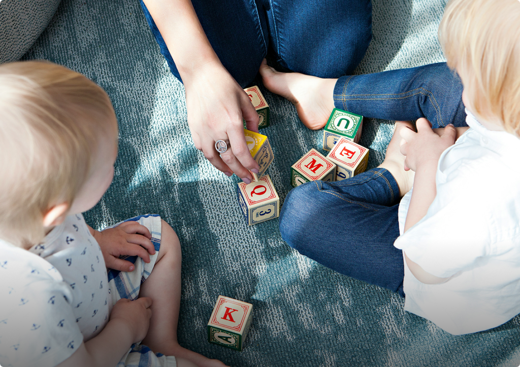 A woman and two children joyfully building structures with colorful blocks on a carpeted floor.