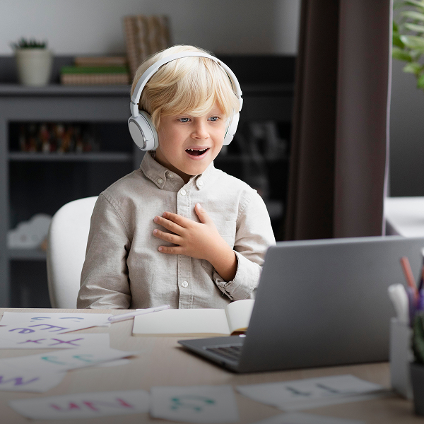 A young boy with headphones sits at a desk, focused on his laptop while engaged in an online activity.
