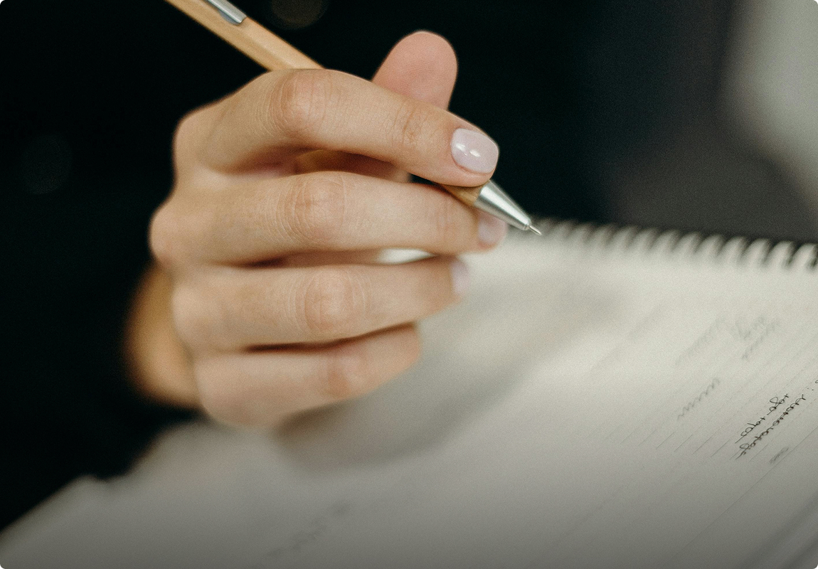 A close-up of a hand writing in a notebook with a pen, capturing the act of note-taking.